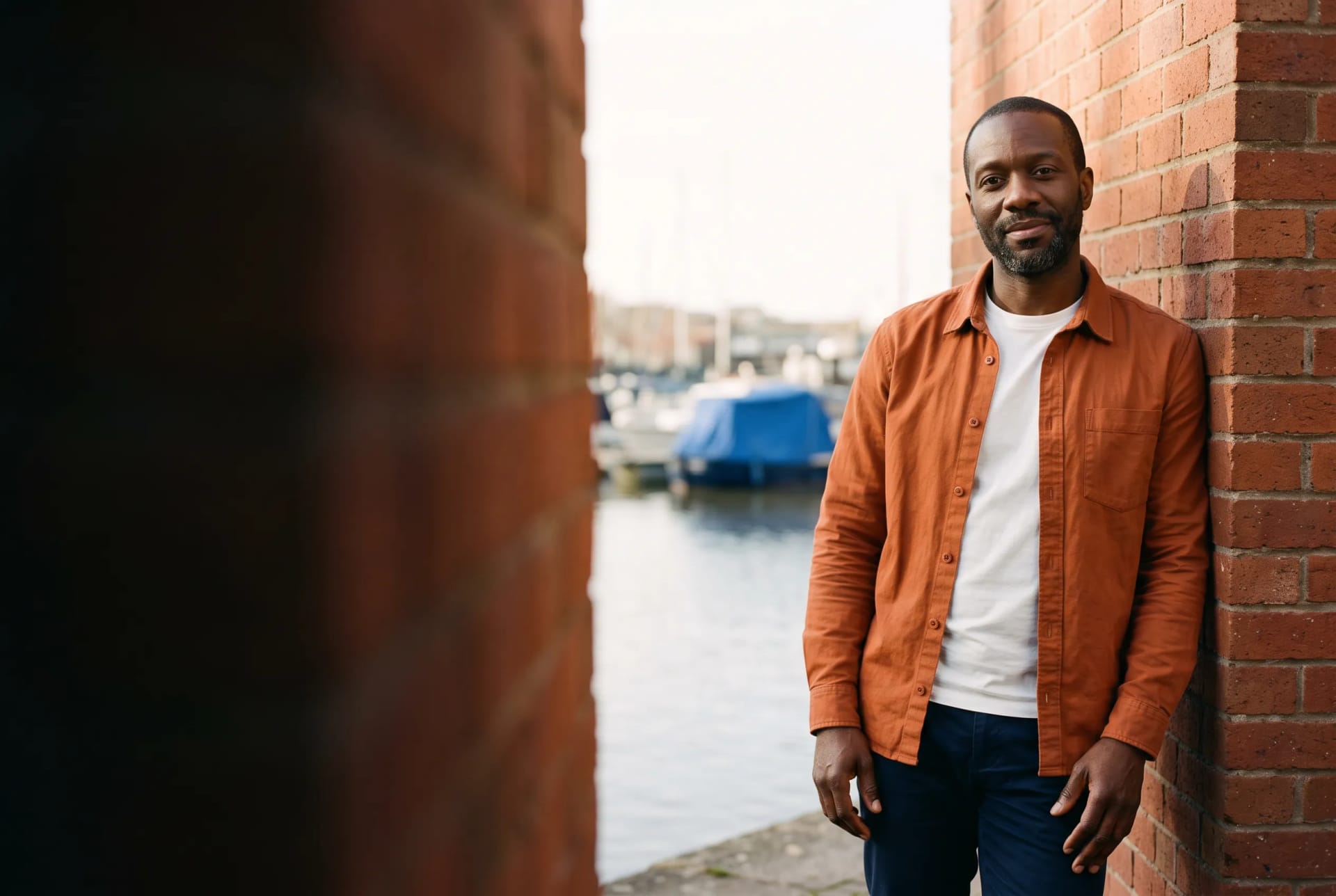 Marcus Grant, psychotherapist, at ease against a warm brick wall near the harbourside in Bristol